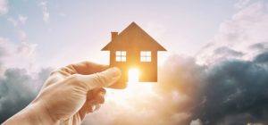 Man's hand holds wooden flat house against the sun